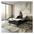 Woman sitting on adjustable Ergonomic mattress in a modern bedroom with large windows and a cityscape view.